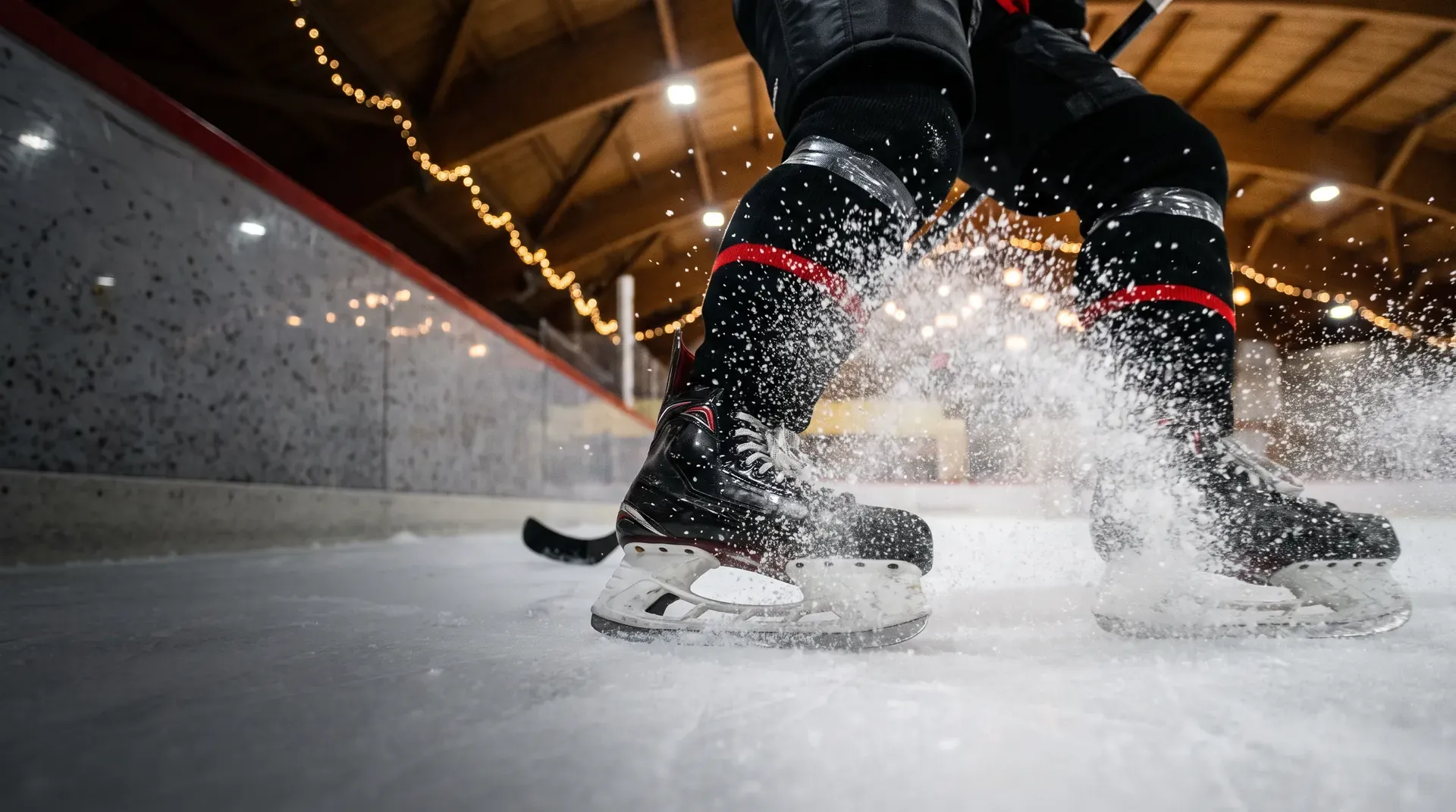 Gli scarponi di un giocatore di hockey che frena sul ghiaccio, con la neve di ghiaccio che schizza, sotto il tetto di legno del palazzetto.