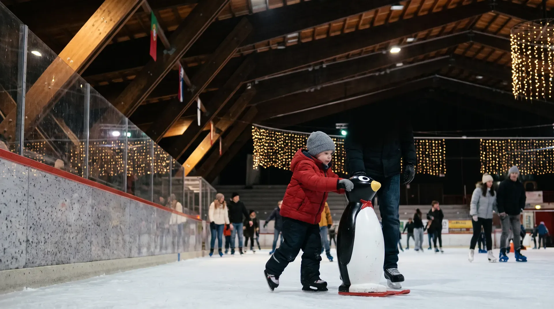 Un bambino con la giacca rossa si regge a un supporto a forma di pinguino, sul ghiaccio.